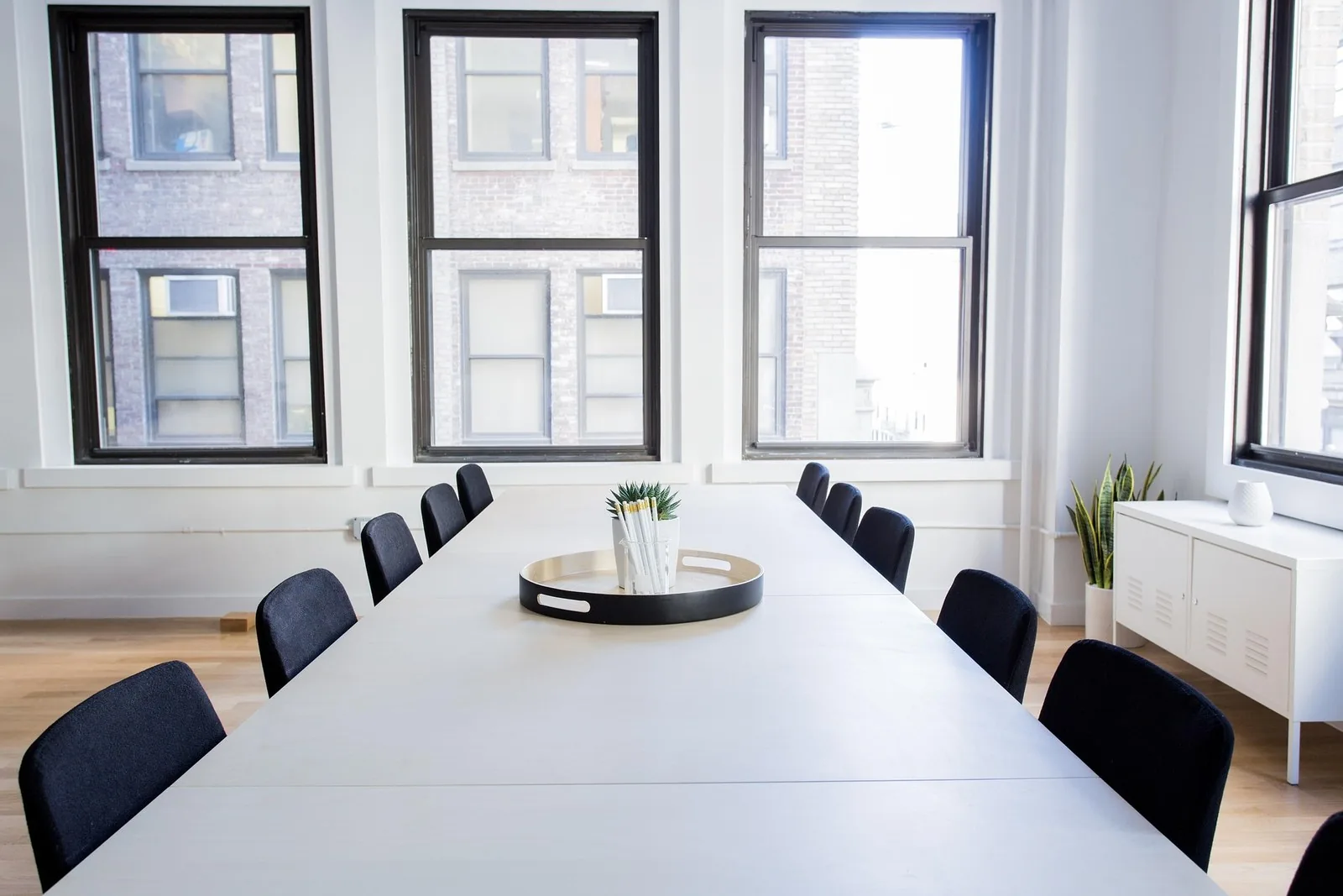 An empty boardroom with chairs along both sides of a long table beneath tall windows.